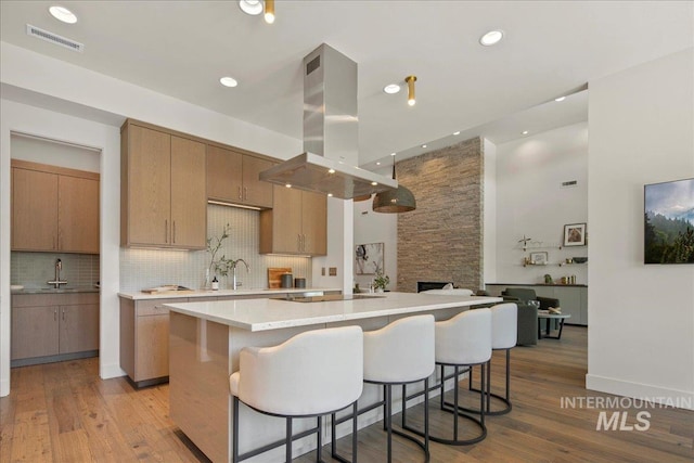 kitchen with island range hood, backsplash, light countertops, a center island, and light wood-style flooring
