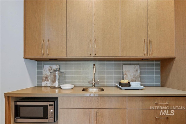 kitchen view of stainless steel microwave, a sink, light countertops, and decorative backsplash