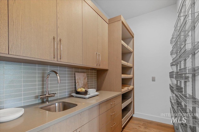 kitchen with a sink, tasteful backsplash, light wood-type flooring, light countertops, and baseboards