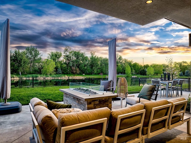 patio terrace at dusk featuring an outdoor living space with a fire pit, view of wooded area, and outdoor dining space