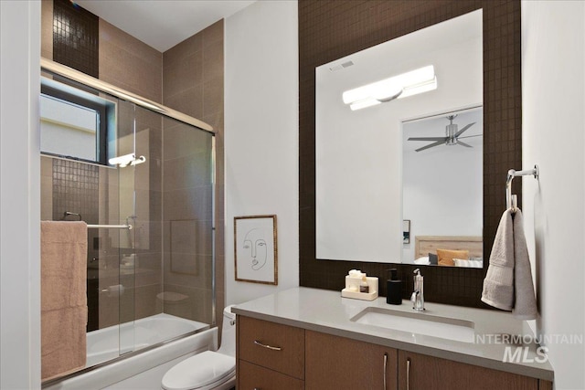 bathroom with toilet, combined bath / shower with glass door, vanity, and a ceiling fan