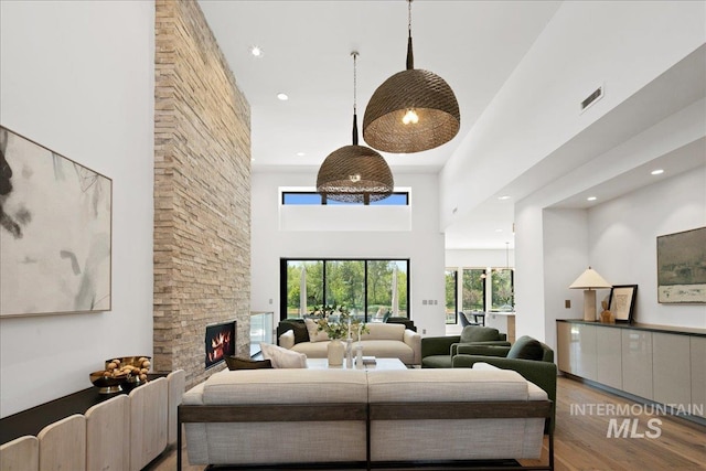 living area featuring wood finished floors, a stone fireplace, a towering ceiling, and recessed lighting