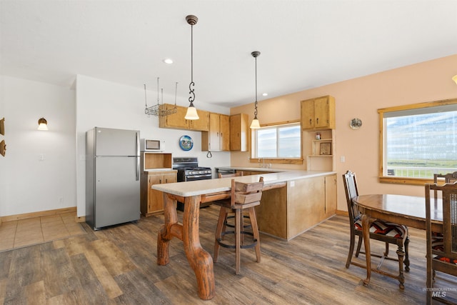 kitchen featuring hanging light fixtures, stainless steel appliances, kitchen peninsula, and hardwood / wood-style flooring