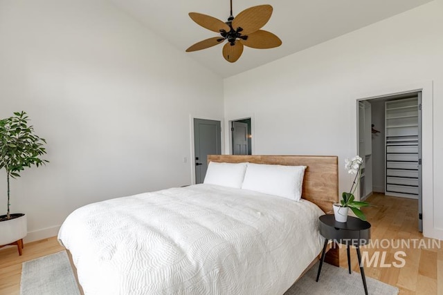 bedroom with high vaulted ceiling, light wood-style floors, baseboards, a walk in closet, and ceiling fan