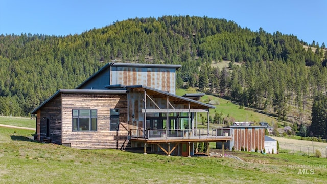back of house with a view of trees, a deck with mountain view, a yard, and a sunroom