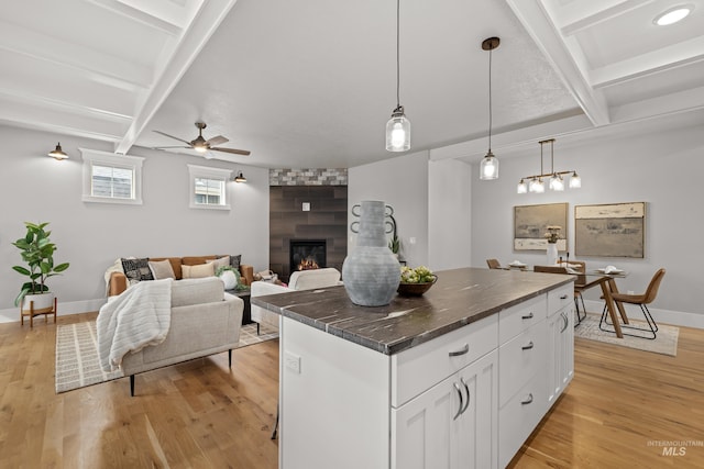 kitchen featuring dark countertops, beamed ceiling, light wood-type flooring, a fireplace, and white cabinetry