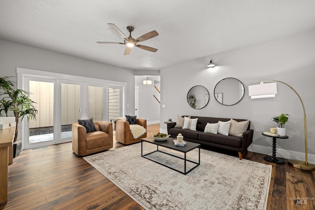 living area featuring dark wood-style floors, visible vents, a ceiling fan, baseboards, and stairs