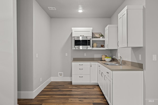 kitchen featuring baseboards, dark wood-style floors, stainless steel microwave, open shelves, and a sink