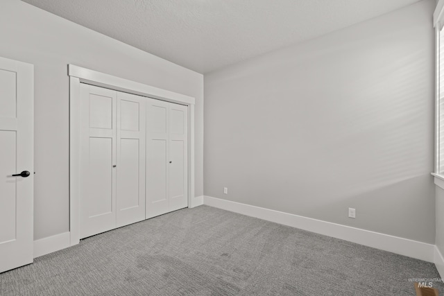 unfurnished bedroom with carpet floors, a closet, baseboards, and a textured ceiling