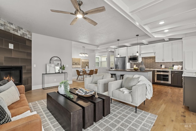 living area with a large fireplace, light wood-style flooring, ceiling fan, and beam ceiling