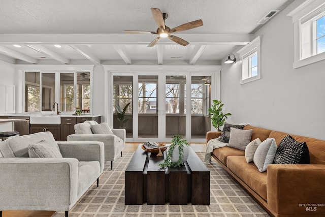 living room with a ceiling fan, visible vents, beamed ceiling, and a textured ceiling