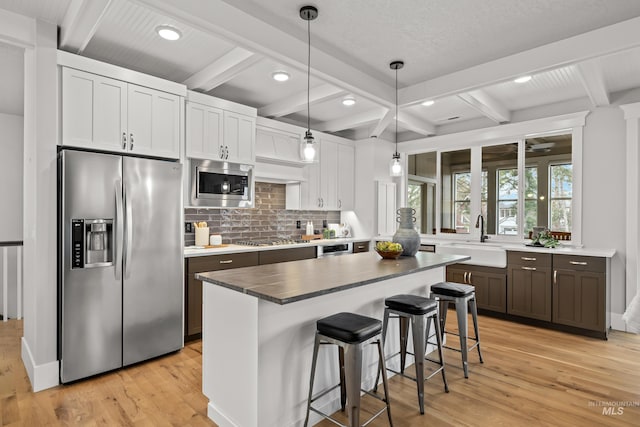 kitchen with light wood finished floors, decorative backsplash, a breakfast bar, stainless steel appliances, and a sink