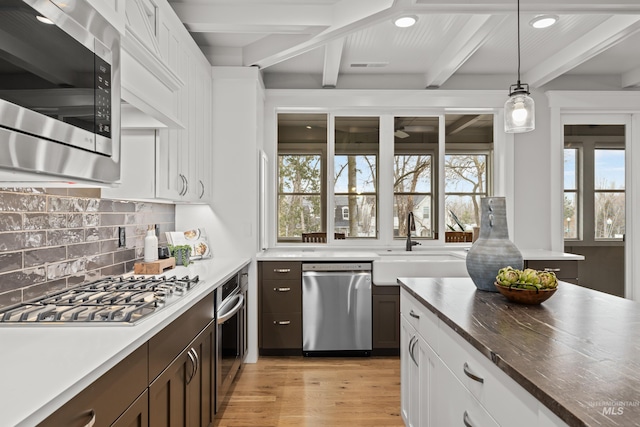 kitchen with light wood-style flooring, appliances with stainless steel finishes, beam ceiling, decorative backsplash, and pendant lighting