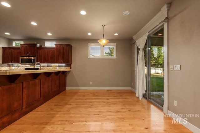 kitchen featuring pendant lighting, a kitchen breakfast bar, light hardwood / wood-style floors, decorative backsplash, and kitchen peninsula