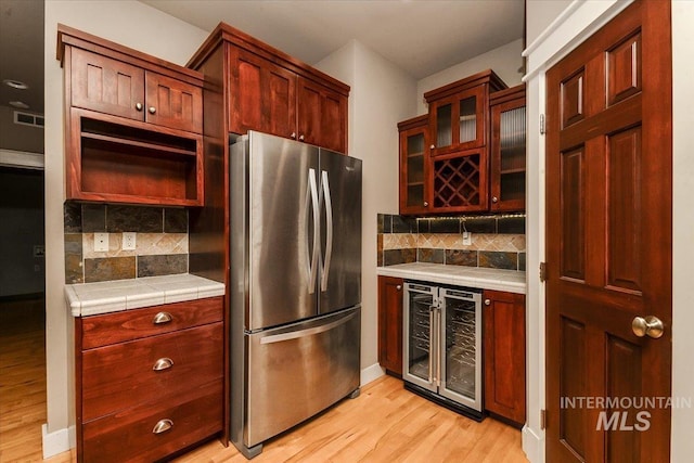 kitchen featuring wine cooler, tile countertops, stainless steel fridge, light hardwood / wood-style floors, and decorative backsplash