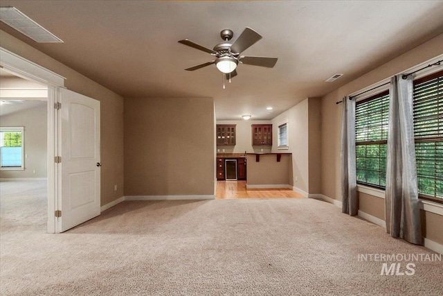 unfurnished living room with light carpet, a healthy amount of sunlight, ceiling fan, and bar