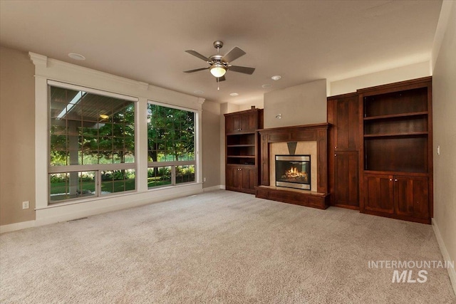 unfurnished living room featuring ceiling fan, light colored carpet, and a high end fireplace