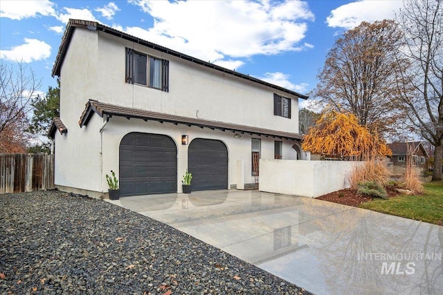 view of front facade with a garage, fence, stucco siding, and concrete driveway