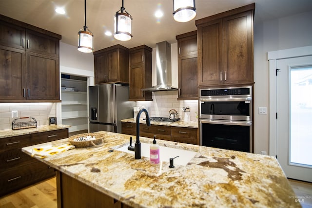 kitchen with decorative light fixtures, stainless steel appliances, light stone countertops, dark brown cabinets, and wall chimney range hood