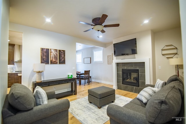 living room featuring ceiling fan, light hardwood / wood-style floors, and a tile fireplace