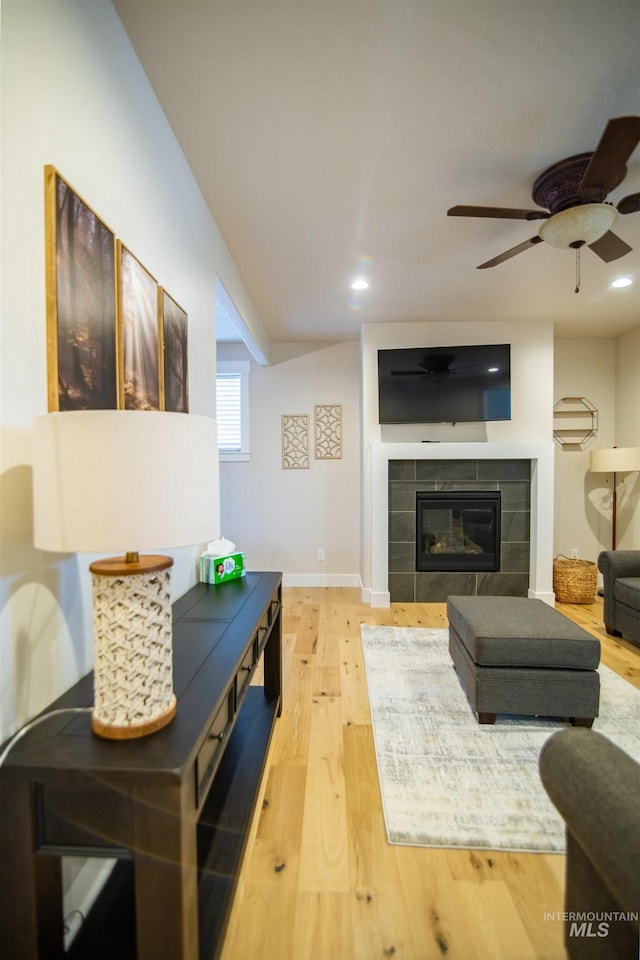 living room with a tiled fireplace, hardwood / wood-style floors, and ceiling fan