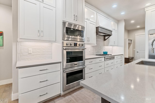 kitchen featuring decorative backsplash, appliances with stainless steel finishes, white cabinetry, light stone countertops, and light wood-type flooring