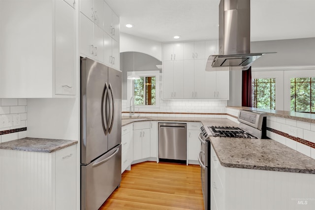 kitchen with island exhaust hood, white cabinets, light hardwood / wood-style floors, and appliances with stainless steel finishes