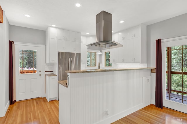 kitchen with white cabinets, light hardwood / wood-style flooring, stainless steel fridge, kitchen peninsula, and island exhaust hood