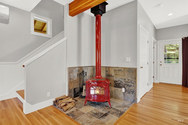 interior space featuring wood-type flooring, a wood stove, an AC wall unit, and beam ceiling