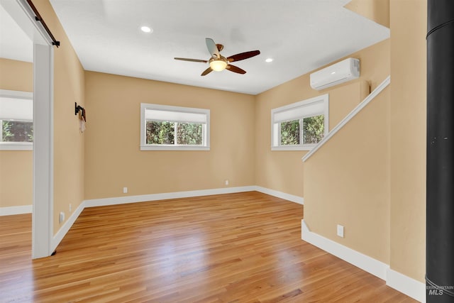 unfurnished room with a wall mounted AC, light hardwood / wood-style flooring, a healthy amount of sunlight, and a barn door