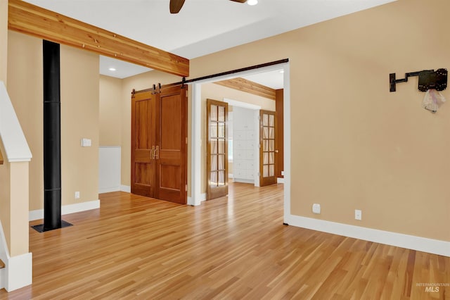 unfurnished room featuring beam ceiling, a barn door, ceiling fan, and light hardwood / wood-style floors
