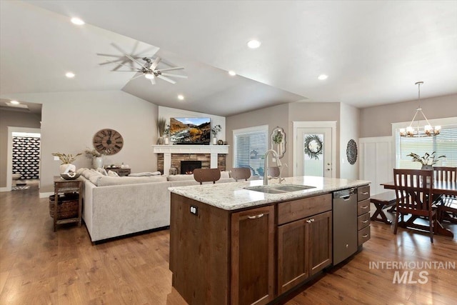 kitchen with sink, light hardwood / wood-style flooring, a center island with sink, a stone fireplace, and stainless steel dishwasher