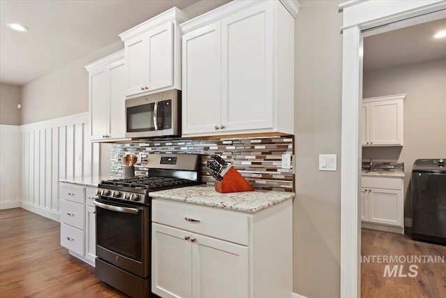 kitchen featuring white cabinetry, backsplash, stainless steel appliances, light stone countertops, and light hardwood / wood-style flooring