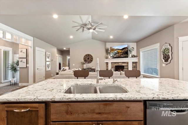 kitchen featuring sink, light stone counters, vaulted ceiling, dishwasher, and a fireplace