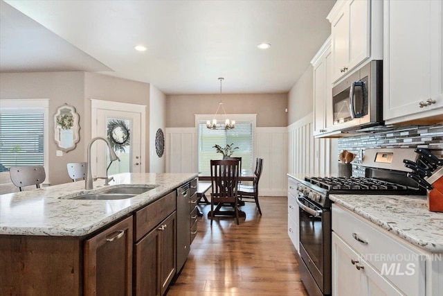 kitchen featuring sink, hanging light fixtures, stainless steel appliances, white cabinets, and a center island with sink