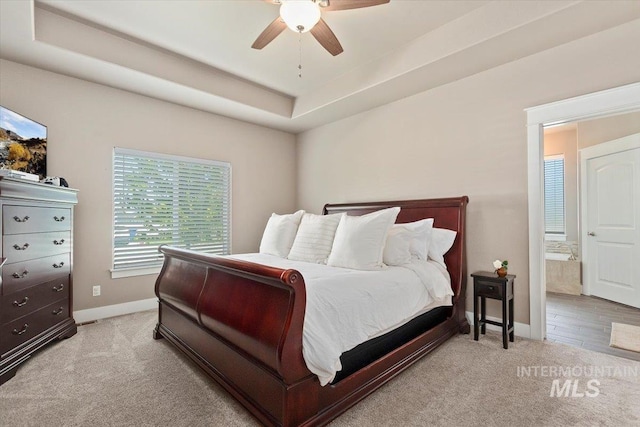 bedroom with ceiling fan, a raised ceiling, light colored carpet, and ensuite bath