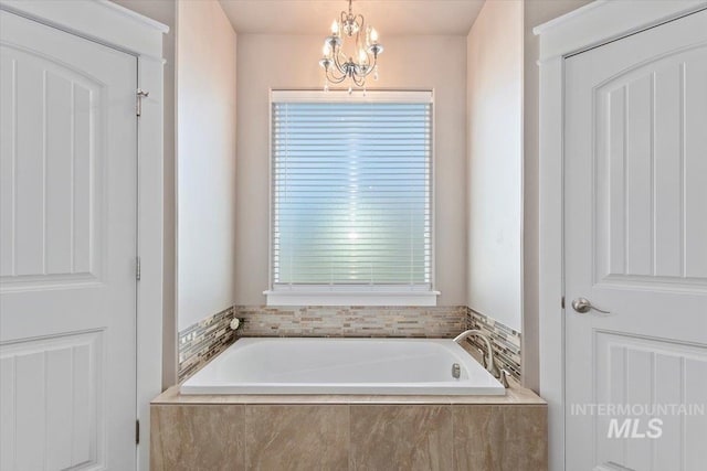 bathroom featuring tiled bath, a chandelier, and a wealth of natural light