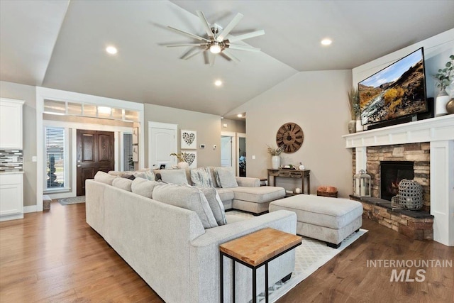 living room featuring ceiling fan, lofted ceiling, a stone fireplace, and wood-type flooring