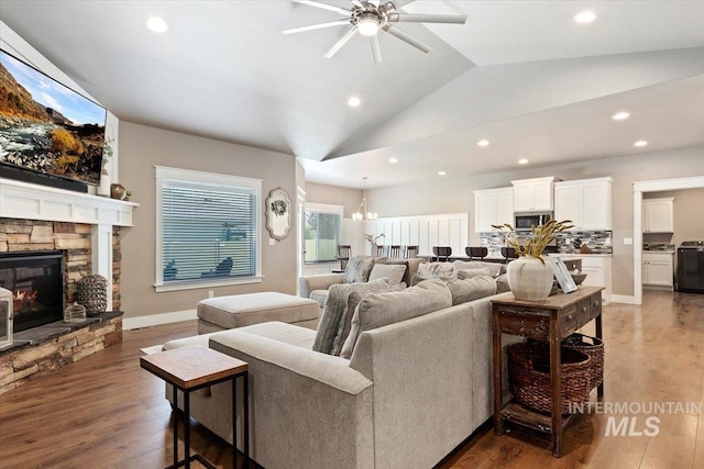 living room with a fireplace, dark wood-type flooring, vaulted ceiling, and ceiling fan with notable chandelier