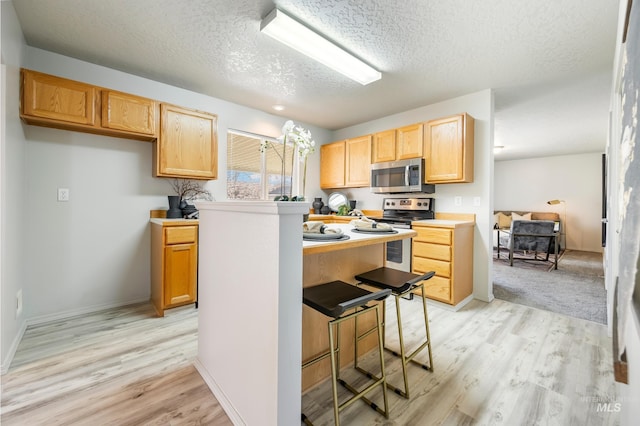 kitchen with a textured ceiling, stainless steel appliances, light hardwood / wood-style flooring, and light brown cabinetry