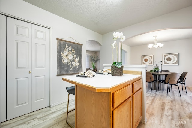 kitchen featuring a center island, an inviting chandelier, a textured ceiling, light hardwood / wood-style flooring, and hanging light fixtures