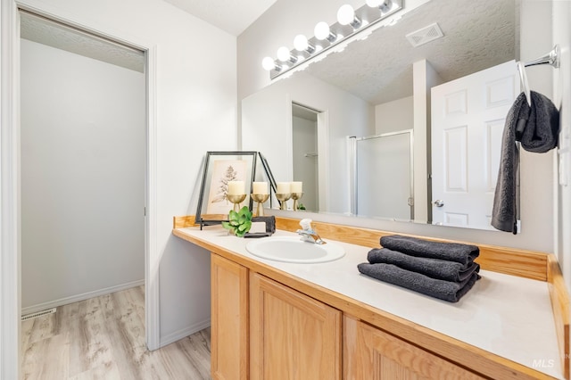 bathroom with hardwood / wood-style flooring, a shower with door, a textured ceiling, and vanity