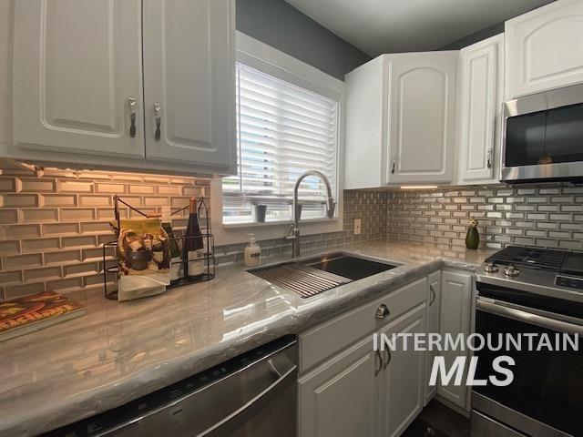 kitchen with appliances with stainless steel finishes, a sink, white cabinetry, and tasteful backsplash