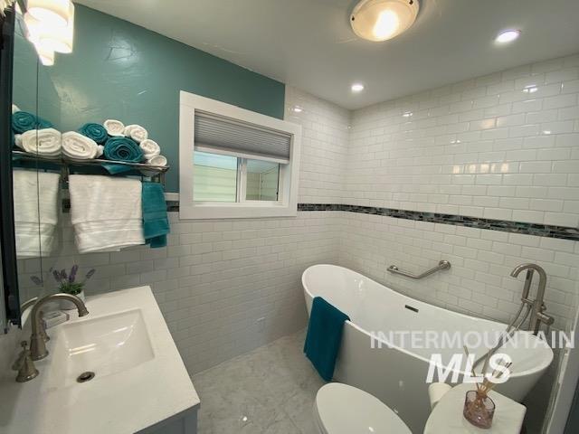 bathroom with vanity, tile walls, a freestanding bath, recessed lighting, and toilet
