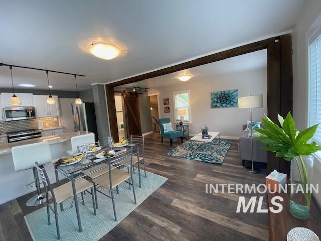 dining space with dark wood-type flooring, baseboards, rail lighting, and a barn door