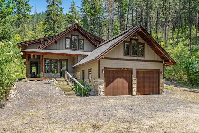 278 Elk Lake Rd, New Meadows, ID 83654 - view of front of property featuring stone siding, gravel driveway, a wooded view, and a garage
