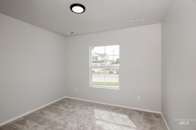 empty room with baseboards, visible vents, and light colored carpet