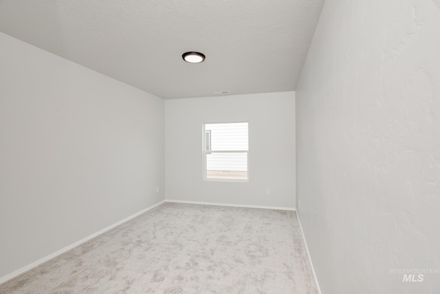 spare room with light carpet, a textured ceiling, and baseboards