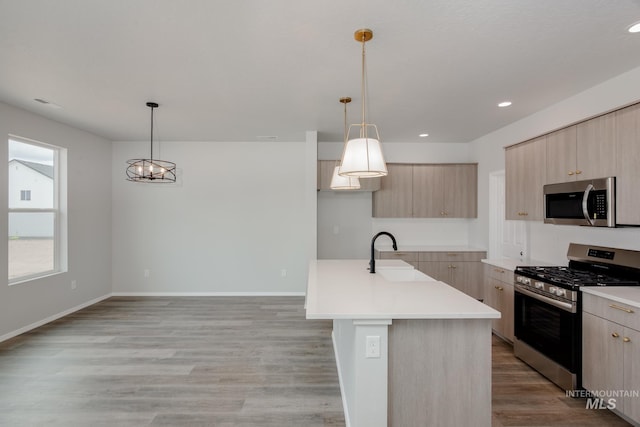 kitchen featuring a sink, light countertops, appliances with stainless steel finishes, an island with sink, and decorative light fixtures