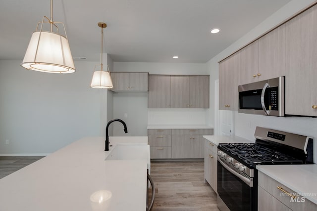 kitchen with light brown cabinets, stainless steel appliances, a sink, hanging light fixtures, and light countertops